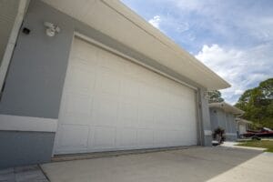 A wide, modern white double garage door on a gray house with a clean concrete driveway.