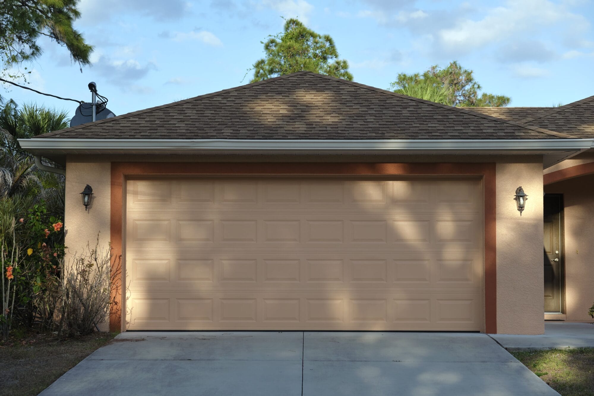 A beige garage door on a residential house with a brown roof and light-colored siding.
