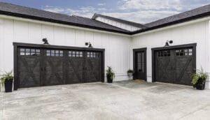 The exterior of a modern home with two dark, wood-look garage doors featuring cross-buck designs and windows.