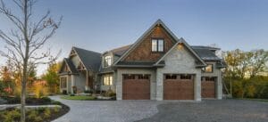 Luxury Craftsman style home with three dark brown carriage house garage doors and light gray stone and wood shake siding, illustrating modern garage door design.