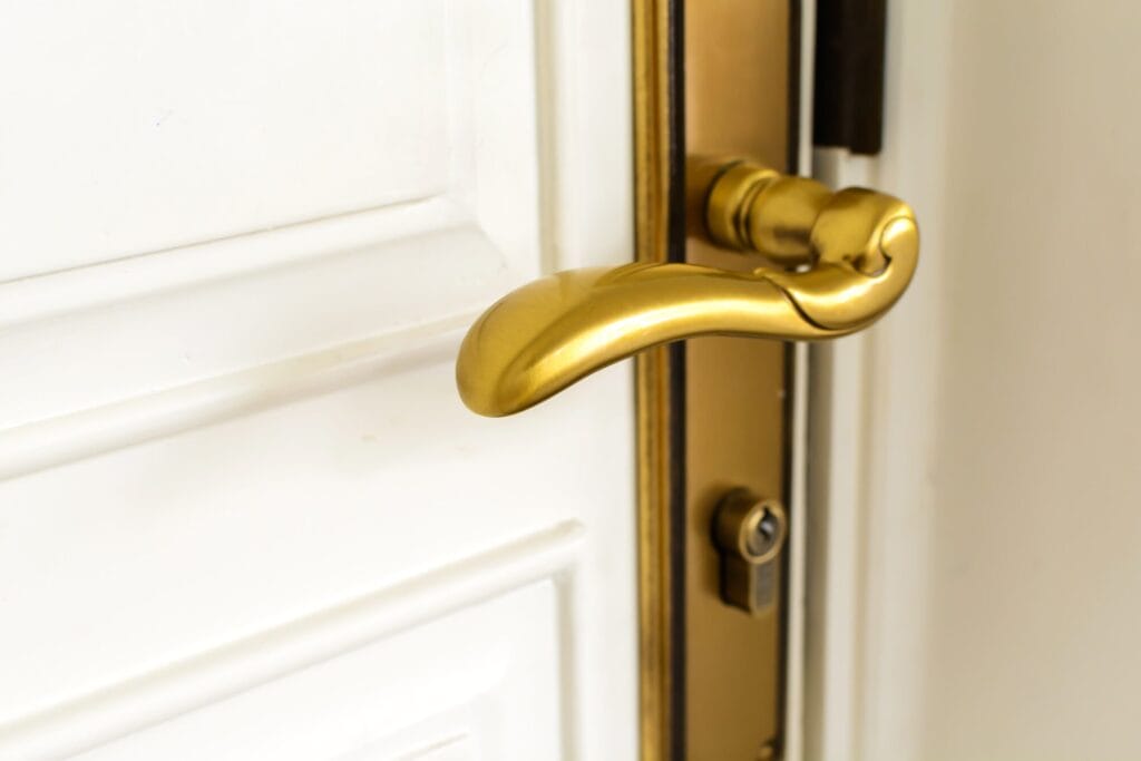 A close-up of a modern, shiny gold-colored door handle and lock on a white panel door.