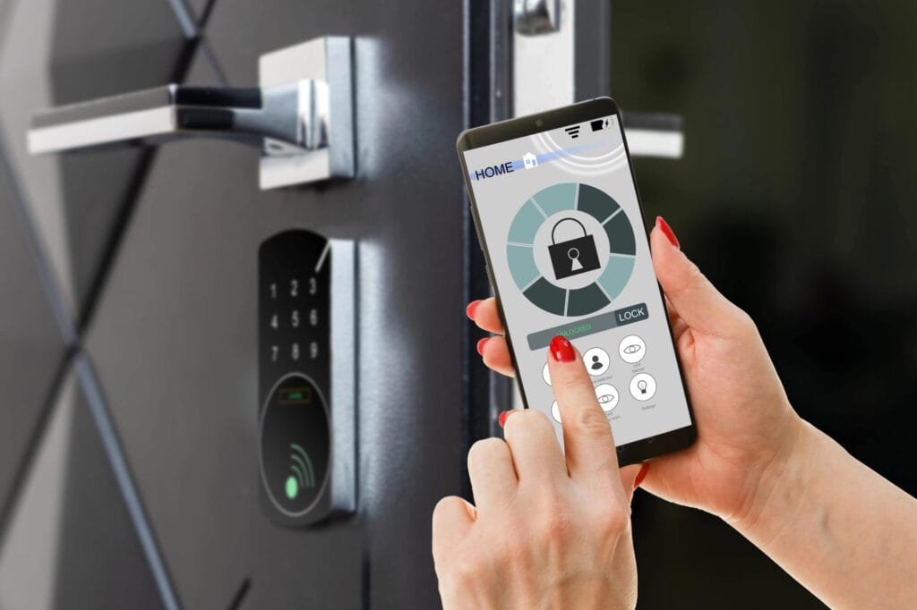 A person's hand is using a smartphone to interact with a home security app interface that shows a locked icon, with a modern smart lock and keypad visible on a door in the background.