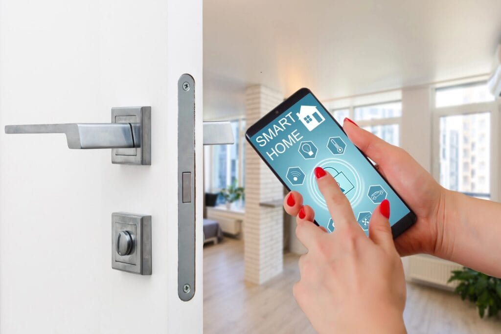 A person's hand with red nail polish is using a smartphone to interact with a smart home app showing a lock screen, with a modern door handle and deadbolt assembly visible next to it.