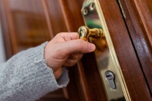 A close-up of a person’s hand attempting to turn the handle of a wooden door, illustrating the need for a locksmith emergency service during a lockout.