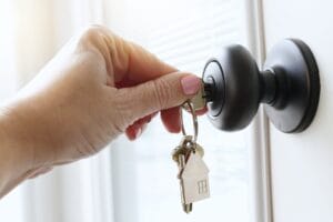 A hand with pink fingernail polish inserting a silver key into a dark bronze doorknob on a white door.