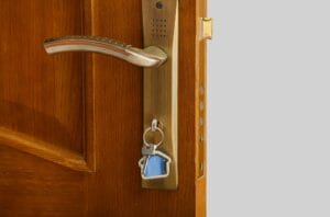 A close-up of a modern wooden door with a brass handle and a key inserted into the cylinder, illustrating one of the many types of door locks discussed in a homeowner's guide.