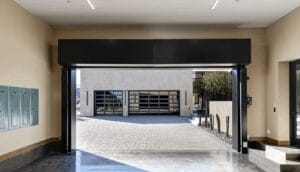A modern luxury garage door opens then closes halfway, revealing an expansive paved driveway and additional glass-paneled garage doors in the background.