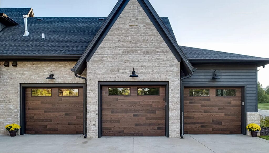 A modern brick home featuring three beautiful wood finish garage doors that require regular maintenance to prevent common garage door issues.