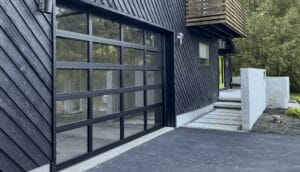 A residential exterior featuring black aluminum glass garage doors built with a rigid structural grid to securely support clear tempered safety panels.
