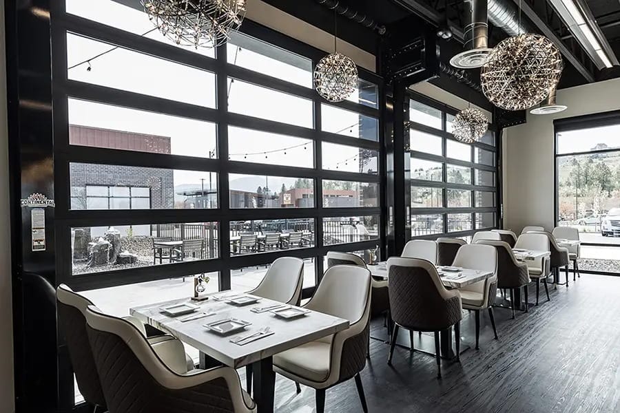 An upscale restaurant interior featuring black-framed commercial glass garage doors that open to an outdoor patio area.