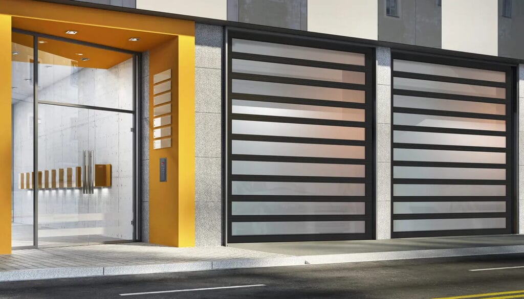 Two sleek black-framed commercial glass garage doors with frosted panels installed on a modern building exterior next to a yellow entryway.